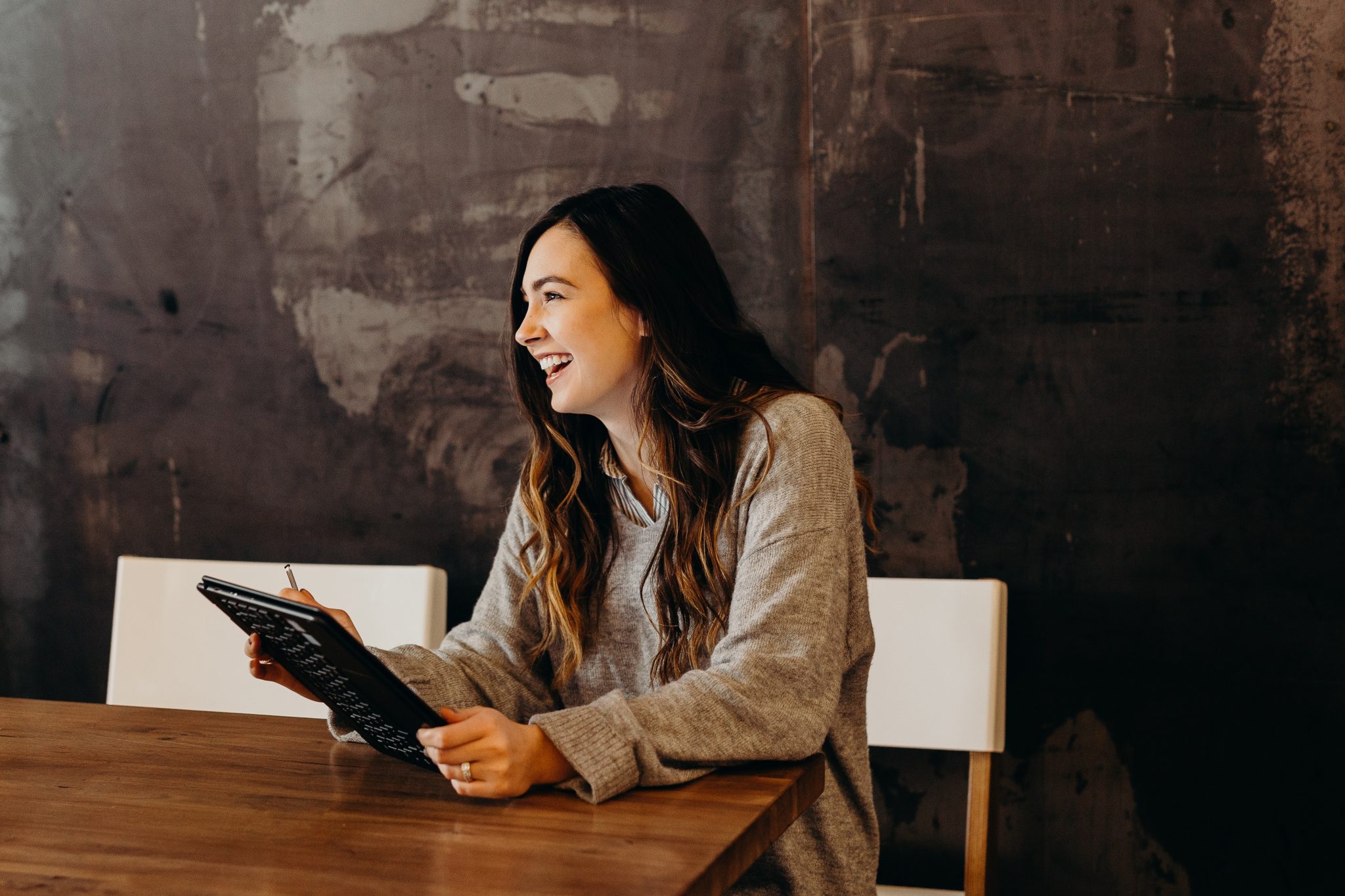 A woman sits at a desk laughing holding a tablet.