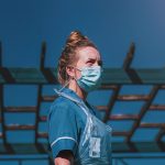 A nurse wearing a mask and PPE stands outside a facility.